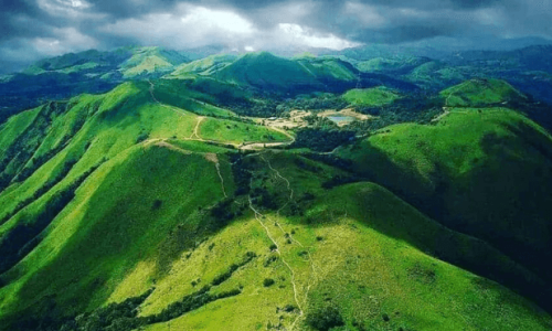 A green mountain range under a dark sky, showcasing the serene beauty of Devaramane Hills in Chikmagalur.