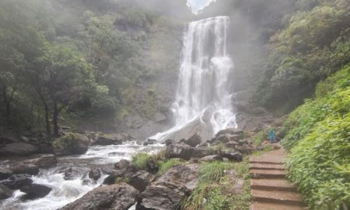 A man walking next to a waterfall on a scenic path.